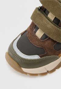 Brązowe i zielone sneakersy z zamszowymi i nylonowymi materiałami, z teksturowaną podeszwą środkową, paskami na rzepy oraz niebieskim akcentem na palcach.