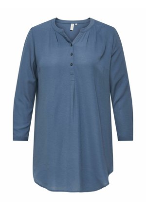 Tunique bleue à manches longues avec un ourlet arrondi, patte de boutonnage et texture subtile. Dotée d'une poche avant et d'un détail plissé au niveau du col.
