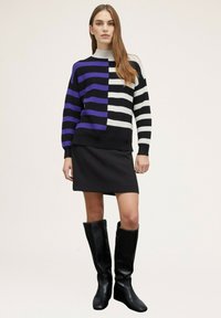 Maglione a righe in nero, bianco e viola, con colletto alto e texture a coste. Abbinato a una mini gonna nera e stivali alti fino al ginocchio.