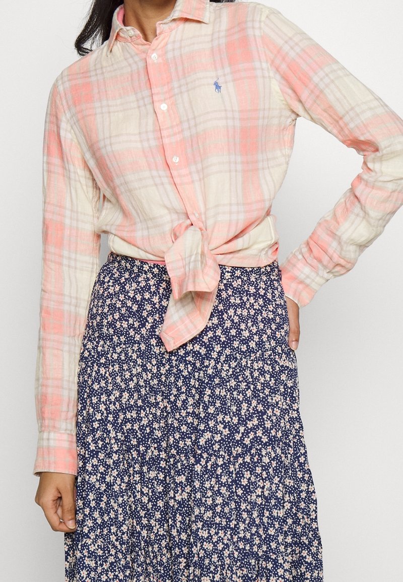 Camisa de cuadros de botones en rosa claro y crema, atada a la cintura, combinada con una falda azul marino con pequeños patrones florales blancos.