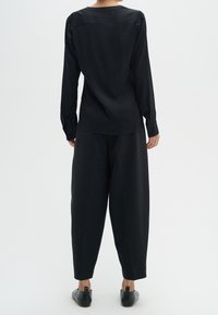 Svart långärmad blus med en smidig yta och avslappnad passform, tillsammans med svarta byxor med vida ben och svarta lågklackade skor.