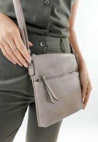 Helle graue Leder-Umhängetasche mit strukturiertem Finish, ausgestattet mit einer vorderen Reißverschlusstasche und einem Handgelenkband. Die Tasche ist flach und rechteckig.