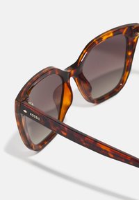 Occhiali da sole tartarugati con grandi montature, lenti scure e logo Fossil sulla tempia. Design elegante con una finitura lucida.