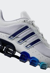Bijela atletska cipela s mrežastim gornjim dijelom, mornarsko plavi i svjetlije plavi naglasci, karakterističan dizajn amortizacije na potplatu i detaljno šivanje.