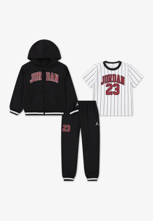 Haut à capuche noir zippé avec le logo "JORDAN", t-shirt rayé blanc avec "JORDAN 23", et pantalon de survêtement noir avec logo et numéro 23.