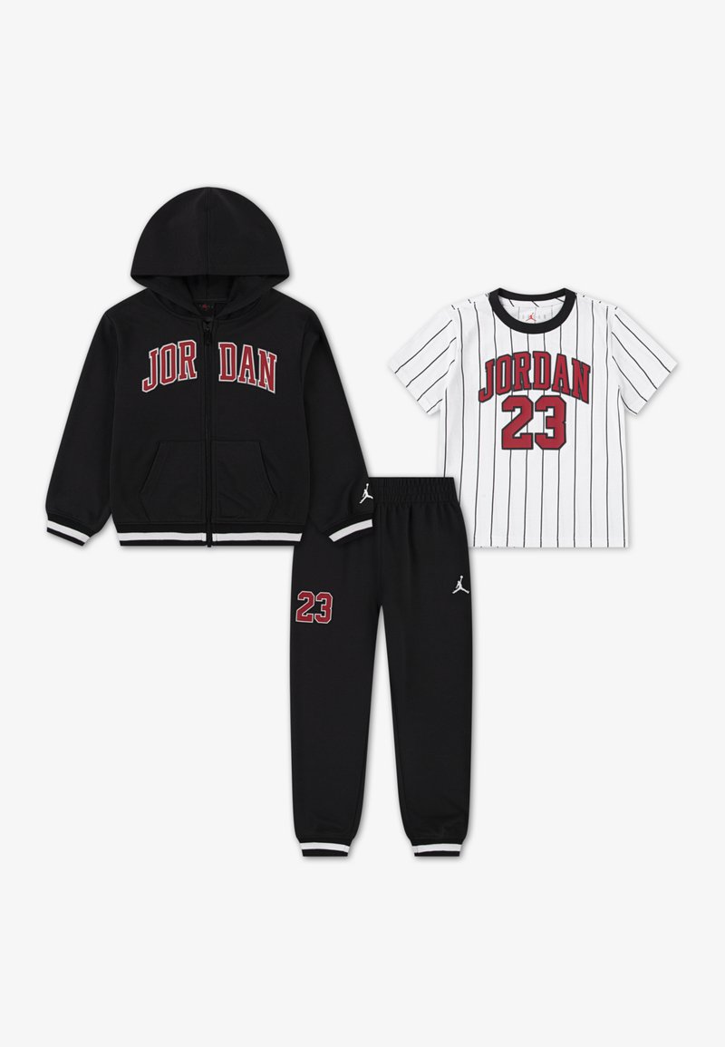 Melna kapuce ar rāvējslēdzēju un "JORDAN" logo, balta T-kreklu ar svītrām un "JORDAN 23," un melnas sporta bikses ar logo un numuru 23.