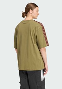 Zelené oversize tričko odstínu olivové, s krátkými rukávy, s bordó pruhovanými akcenty na ramenou a měkkou bavlněnou texturou.