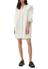 Weißes Baumwollkleid mit puffärmel und Rüschendetails, verziert mit gestickten Akzenten und einem lässigen Schnitt. Tragen mit schwarzen Plateau-Sandalen.