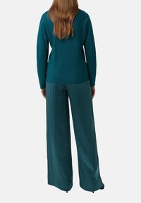 Turkusowy, luźny sweter o błyszcz�ącej fakturze, zestawiony z szerokimi spodniami w dopasowanym turkusowym odcieniu, obydwa o gładkiej powierzchni.