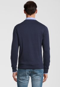 Marineblauwe trui met een ronde halslijn en lange mouwen, voorzien van een geribbelde onderrand en manchetten, gedragen met een lichtblauwe kraagshirt eronder.