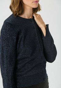 Cardigan bleumarin dintr-un material texturat și strălucitor, cu decolteu zimțat și închidere cu butoane, având manșete și tiv din bumbac ribbed.