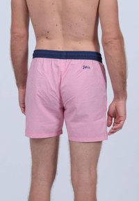 Shorts de bain rayés rouges et blancs avec une taille élastique marine. Présente un petit logo à l'arrière de la taille et une coupe décontractée.