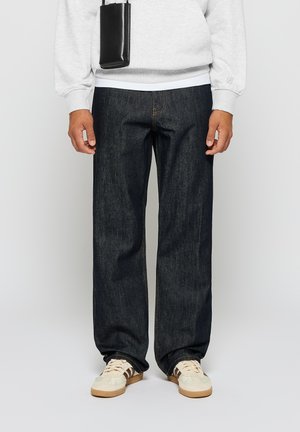 Jeans de mezclilla azul oscuro con un corte recto, que presentan un bordado sutil y una tela de peso medio. Combinados con zapatillas crema y una sudadera gris.