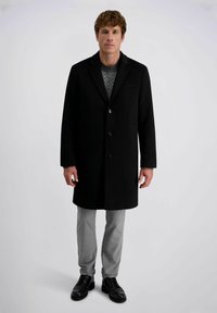 Zwarte wollen overjas met ingezette kraag, enkelvoudig knoopdesign en drie knopen. Draagt over een gebreid patroontrui en grijze broek.