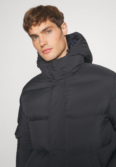Black puffer jacket with a high collar, featuring quilted sections and a zip closure. Smooth, shiny texture, and a fitted silhouette.