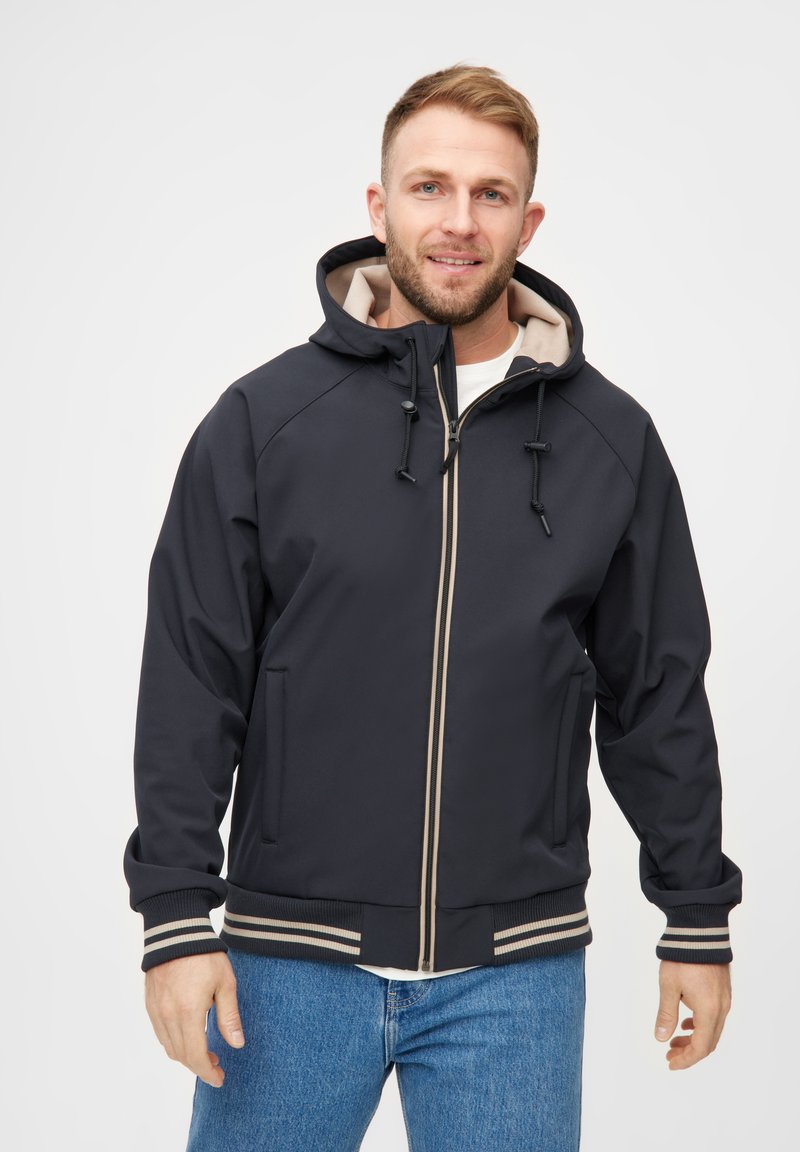 Veste coupe-vent marine avec un intérieur beige, fermeture éclair, cordons de serrage réglables et poignets à rayures côtelées. Deux poches avant sont présentes.
