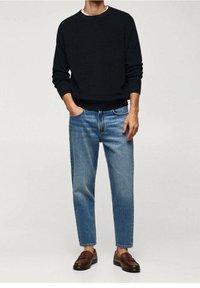 Pull côtelé bleu foncé, jean délavé clair à coupe décontractée, et mocassins marron. Détails remarquables : texture en maille et revers sur les jambes du jean.