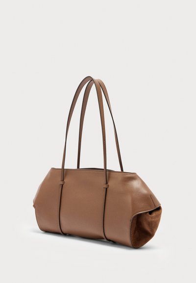 Καφέ δερμάτινη τσάντα χειρός με μακριές, λεπτές λουρίδες και απαλά, στρογγυλεμένα πλαϊνά, εμφανιζόμενη μπροστά σε ένα απλό ανοιχτό φόντο.