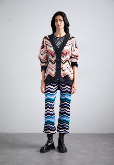 Cardigan tricotat cu model zigzag în roz, negru și crem, asortat cu pantaloni cu model chevron în albastru, negru și violet. Botine negre.