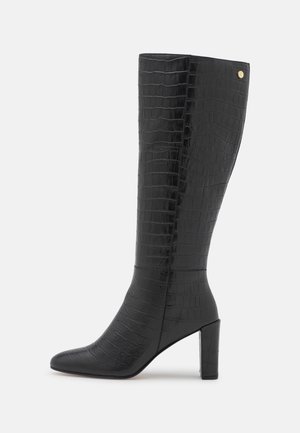 Botte noire montant jusqu'au genou avec texture crocodile, bout pointu, talon bloc, et petit logo doré près du bord supérieur.