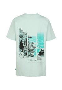 T-shirt in cotone verde menta chiaro con grafica di una costa rocciosa e oceano in nero e turchese, con testo e coordinate in basso.