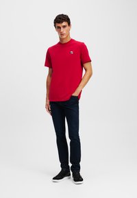 Tricou roșu din bumbac cu guler rotund, mâneci scurte și un accent mic cu logo. Asortat cu blugi bleu închis și adidași negri.