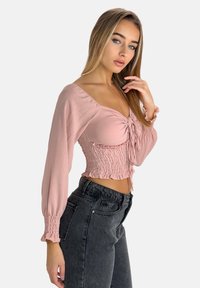 Top corto rosa con maniche lunghe, vita arricciata e dettagli a volant, abbinato a jeans neri a vita alta. Tessuto dalla superficie liscia.