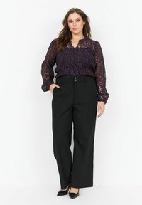 Lilla blonde bluse med V-udskæring og lange, puffede ærmer, parret med højtaljede sorte jakker med striber og sorte spidse hæle.