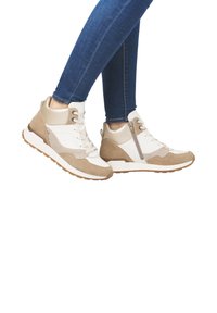 Des baskets montantes en suède crème et beige, avec une fermeture éclair sur le côté, des panneaux texturés et une semelle en caoutchouc. Portées avec un jean bleu.
