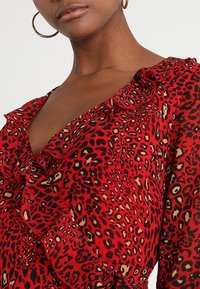 Robe rouge avec un motif léopard, un col à volants et une texture lisse. Comprend des accents noirs et dorés sur un fond vif.