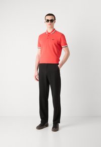 Rød polo skjorte med kontrasterende svart og hvit krage og ermekanter, kombinert med svarte bukser og mørke joggesko.