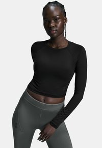 Schwarzes langärmeliges Crop-Top aus einem weichen Material mit rundem Halsausschnitt, kombiniert mit hoch taillierten, dunkelgrünen Leggings mit Seitentaschen.