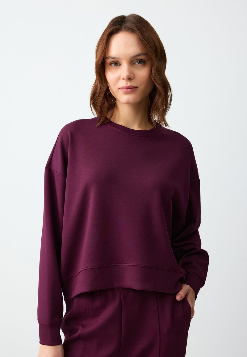 Felpa corta bordeaux con maniche lunghe, scollatura rotonda e polsini a costine. Tessuto morbido e strutturato con vestibilità comoda.