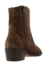 Botín de ante marrón hasta el tobillo con cremallera lateral, tacón bajo y apilado, y una textura suave. Presenta elementos de diseño curvados en el talón y la punta.