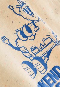 Two blue cartoon characters with large eyes and smiling faces, one waving, printed on speckled cream fabric with partial blue text.