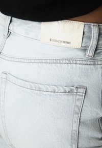 Svetlo modri kavbojki z zadnjim žepom, ki imajo teksturiran bel usnjen etiket, na katerem je vtisnjeno "Stradivarius" in "92."