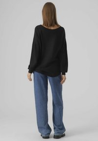 Czarny, oversize'owy sweter z szerokim dekoltem, zestawiony z luźnymi, niebieskimi dżinsami. Gładka faktura i swobodna sylwetka.