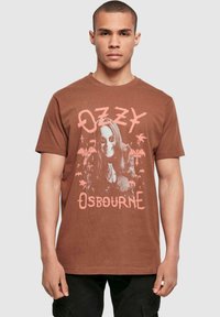 Brown cotton t-shirt featuring a graphic print of a figure with sunglasses, surrounded by bats and palm trees, with "OZZY OSBOURNE" text.