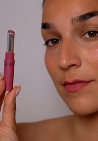 Tuba szminki w delikatnym różu, z srebrnym akcentem na górze, trzymana przez osobę na neutralnym tle; usta w kolorze dopasowanym do szminki o matowym wykończeniu.