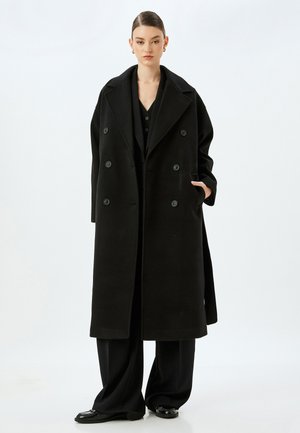 Cappotto in lana nera con design doppiopetto, ampi rever e dettagli con bottoni. Presenta una vestibilità comoda e tasche laterali.