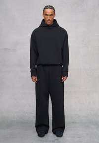 Conjunto de sudadera y pantalones deportivos negros, hechos de una tela suave. Presenta un corte relajado, puños acanalados y una marca sutil en los pantalones.