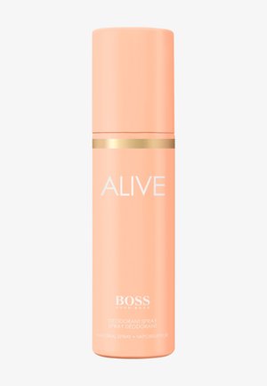 Pfirsichfarbene zylindrische Deospraydose mit goldenem Band, beschriftet mit "ALIVE" und "BOSS HUGO BOSS" auf weißem Hintergrund.