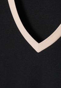 Czarny materiał z dekoltem w serek, ozdobiony kontrastującą jasnobeżową lamówką. Miękka tekstura z czystymi krawędziami i minimalnie widocznymi szwami.