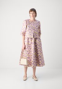 Blomstrete kjole og matchende kort jakke i lavendel og gul. Glatt stoff med trekvart ermer, kombinert med en beige veske.