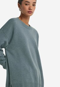 Hellblaues gestricktes Sweatshirt mit Rundhalsausschnitt, überschnittenen Schultern, geripptem Saum und lockerer Passform, das eine weiche Textur zur Schau stellt.
