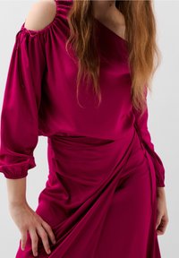 Robe fuchsia à col bateau en tissu léger et lisse, avec un design drapé, des manches froncées et des accents noués à l'épaule.