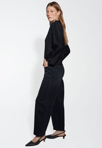 Haut noir scintillant à manches longues, associé à un jean foncé taille haute. Chaussures à talon noir avec bout pointu et détails cloutés.