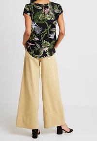 Top negro con estampados botánicos en verde y rosa, combinado con pantalones de pierna ancha beige. Mules negros completan el look.