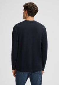 Chemise à manches longues bleu marine avec un col rond et un tissu texturé, associée à un jean en denim, vue de dos.