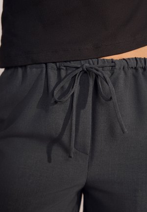 Gros plan sur la taille montrant un pantalon avec une ceinture élastique noire foncée, un cordon de serrage noué et le bord inférieur d'un haut noir côtelé.